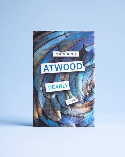 A book titled 'Atwood Dearly Poems' by Margaret Atwood, featuring an abstract blue and brown textured cover, displayed on a light blue background.