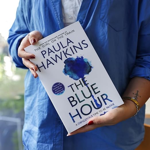Person holding a book titled 'The Blue Hour' by Paula Hawkins